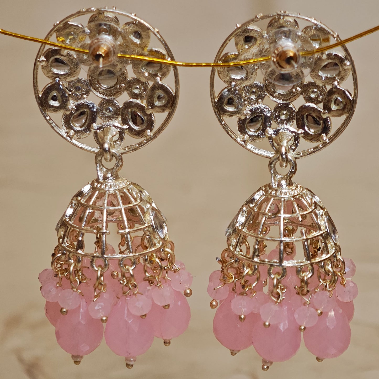 Pair of gold and silver earrings with pink beads on a beige background