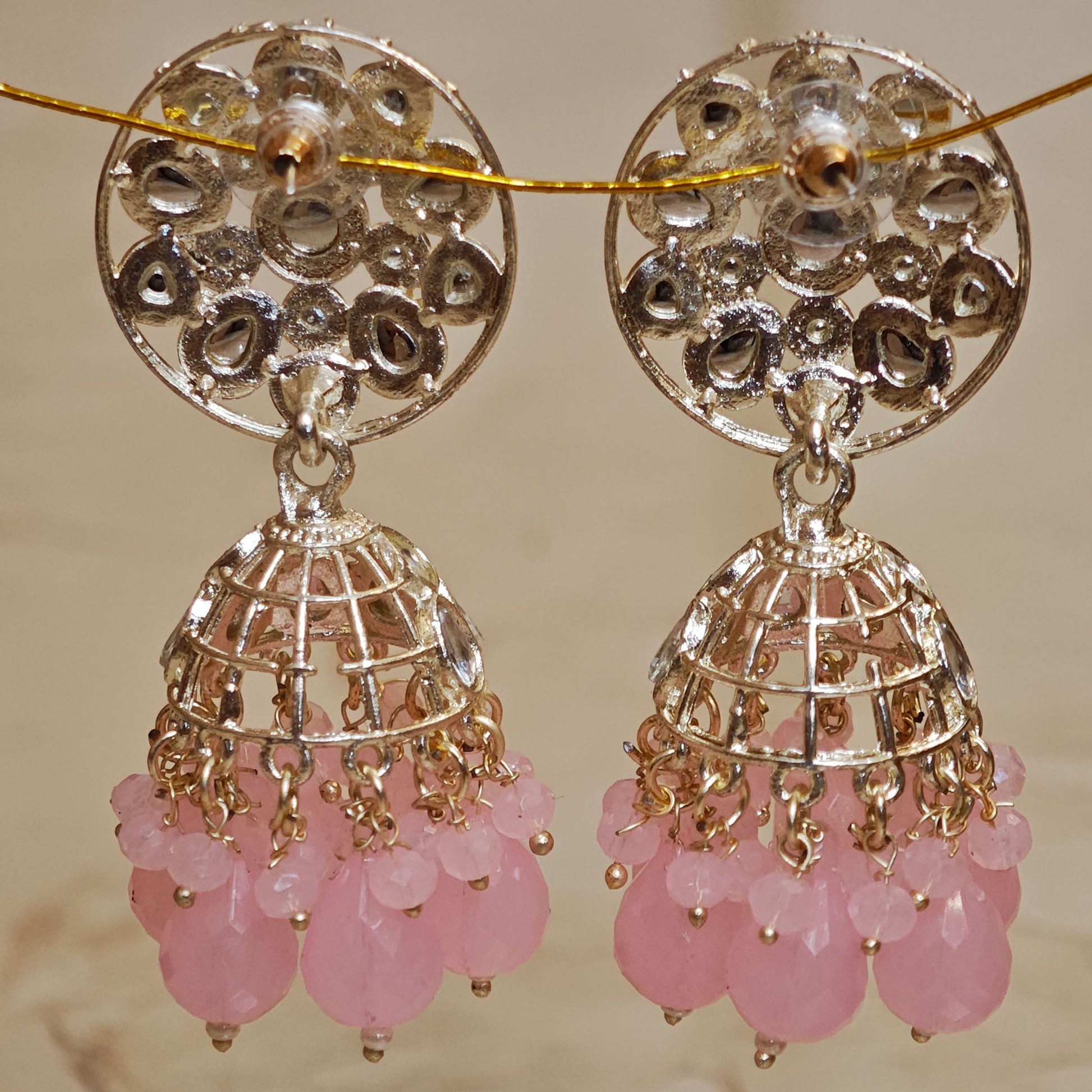 Pair of gold and silver earrings with pink beads on a beige background