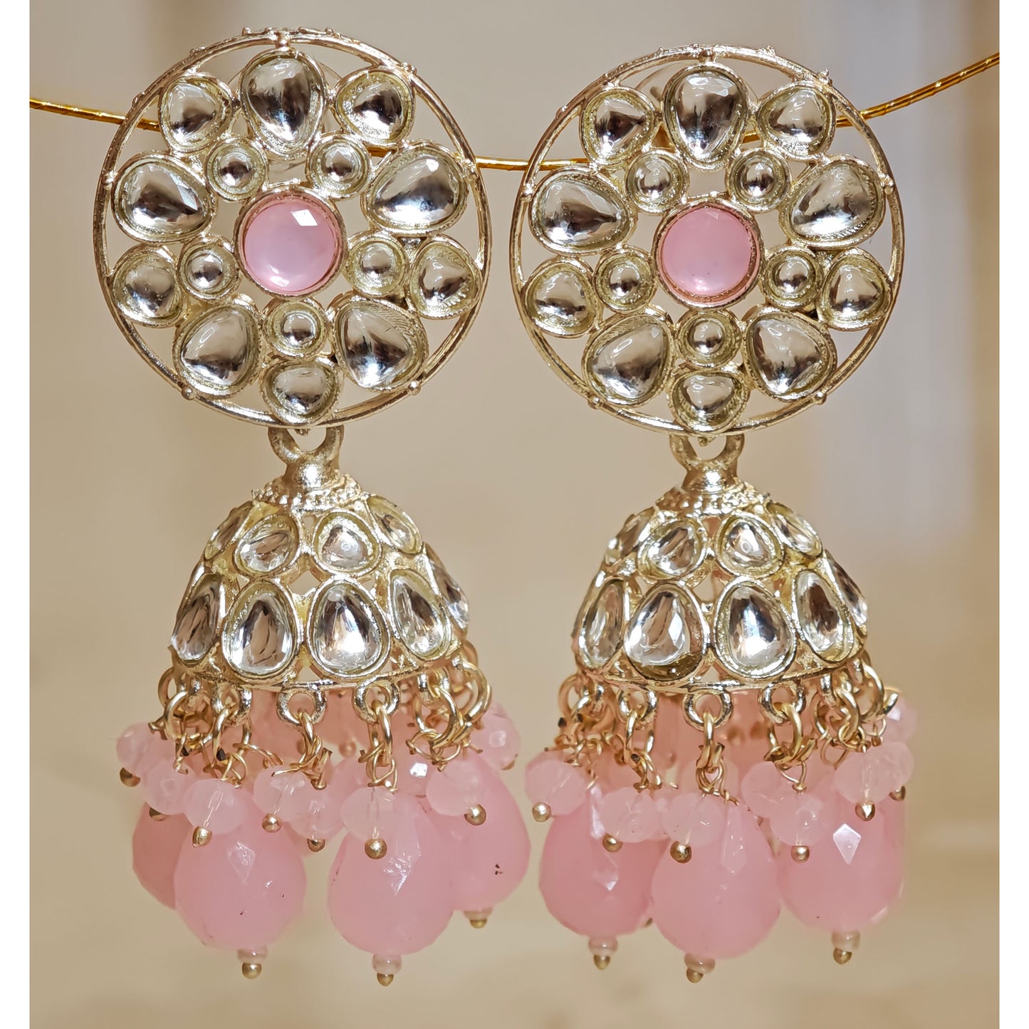 Ornate earrings with pink beads on a beige background
