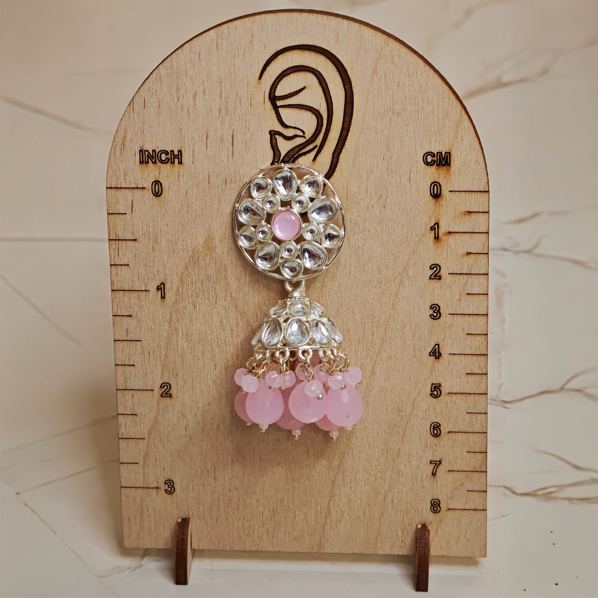 Pink and silver earring on a wooden measurement stand with inch and cm scales.