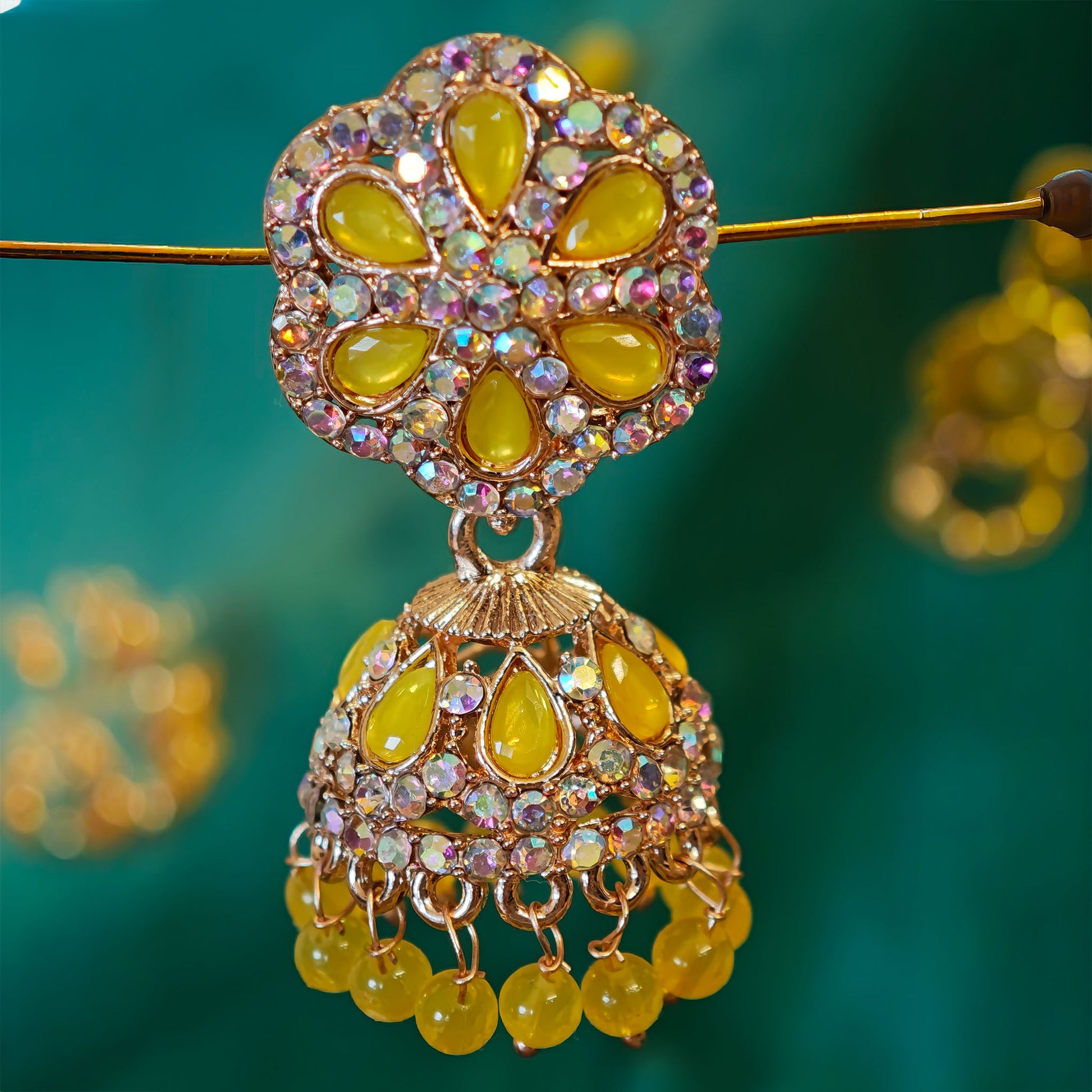 Decorative earring with yellow stones and gold accents on a green background