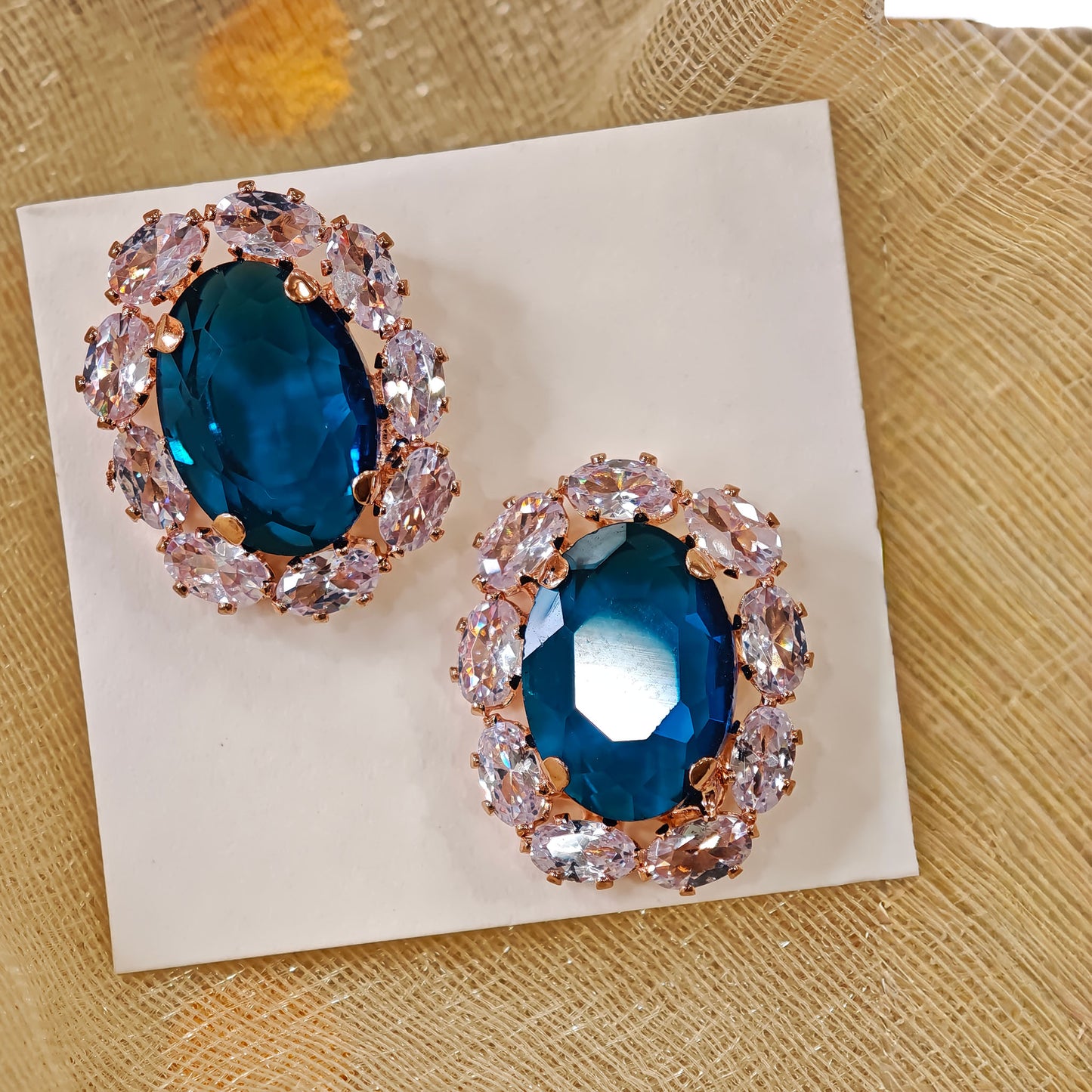 Pair of earrings with blue gemstones and rose gold accents on a beige card.